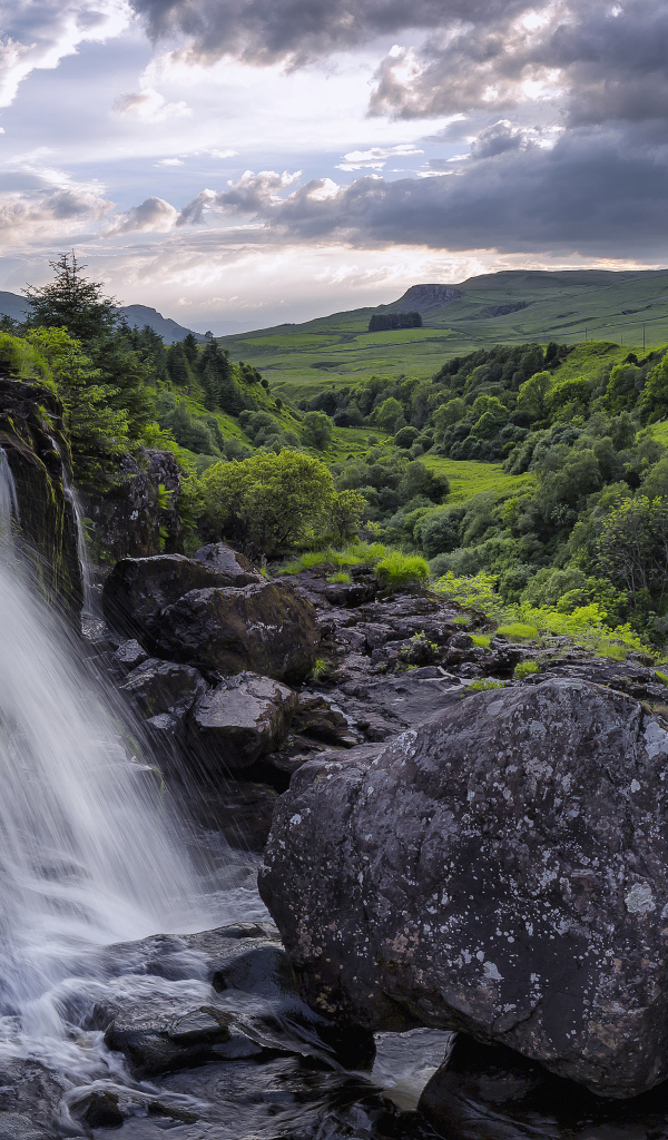 Водопад стекает по камням на фоне красивого неба и зеленого леса
