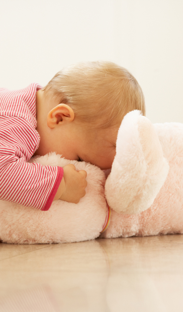 Маленький ребенок играет с розовым игрушечным медведем