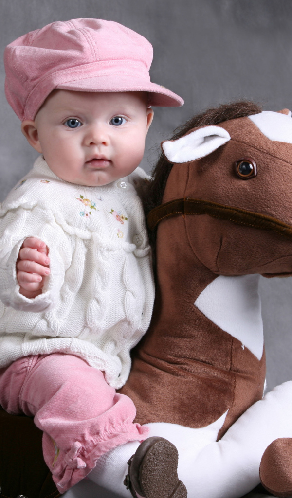 Маленький ребенок в розовой кепке сидит на игрушечной лошади