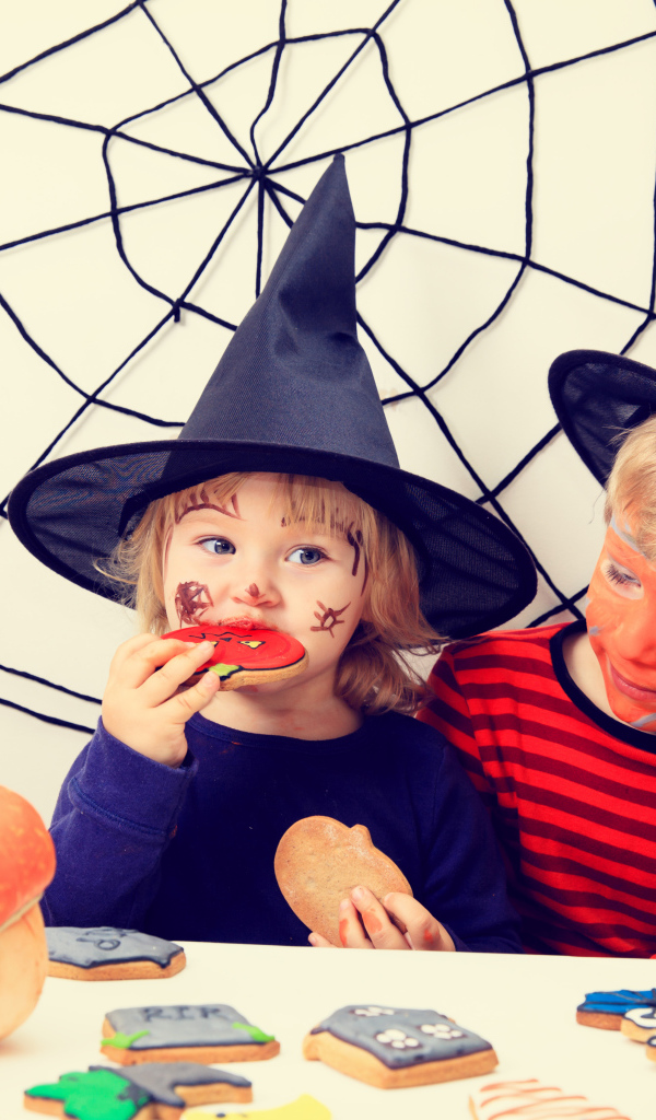 Маленькие дети в костюмах на Хэллоуин едят праздничные сладости