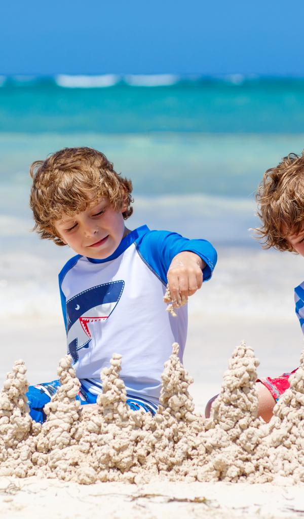 Два маленьких мальчика играют с песком на пляже