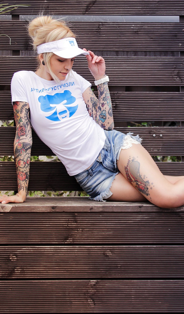 Спортивная девушка в татуировках лежит на деревянной лавке