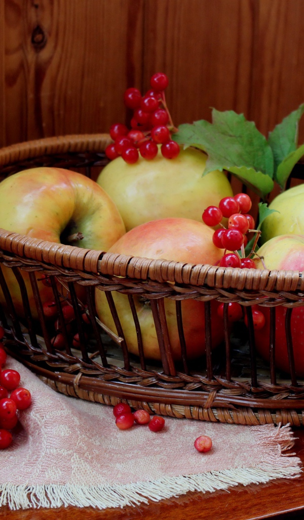 Красивые яблоки в корзине на столе с ягодами калины