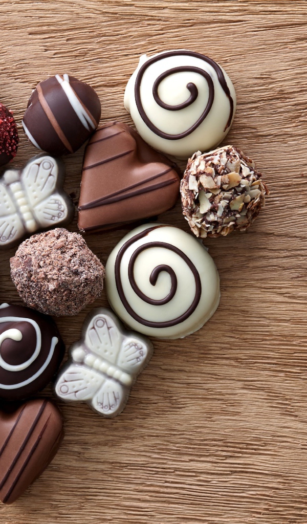 Сердце из шоколадных конфет ассорти на деревянном столе