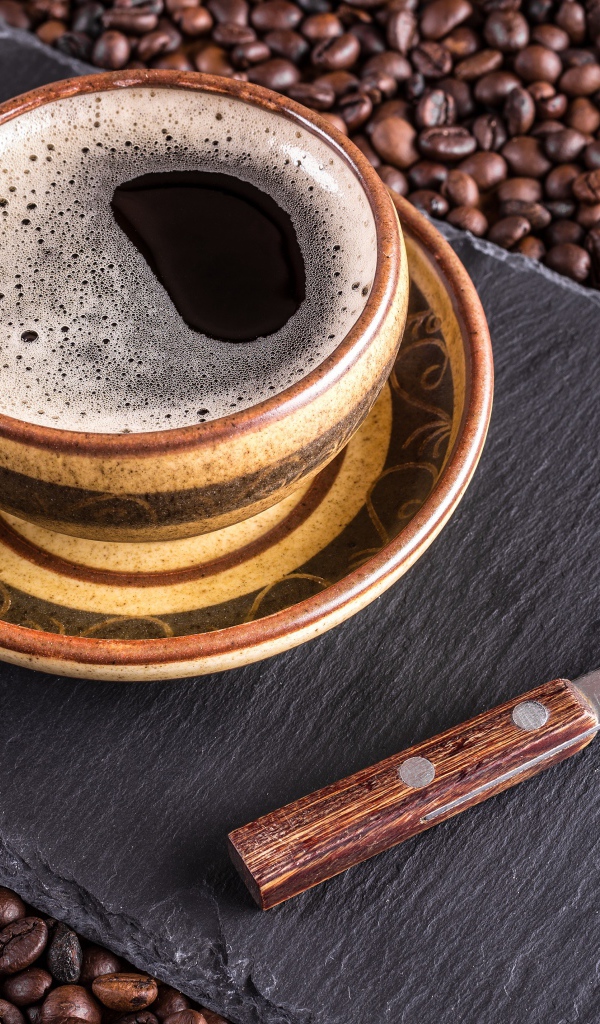 Большая чашка кофе с чайной ложкой стоят на кофейных зернах