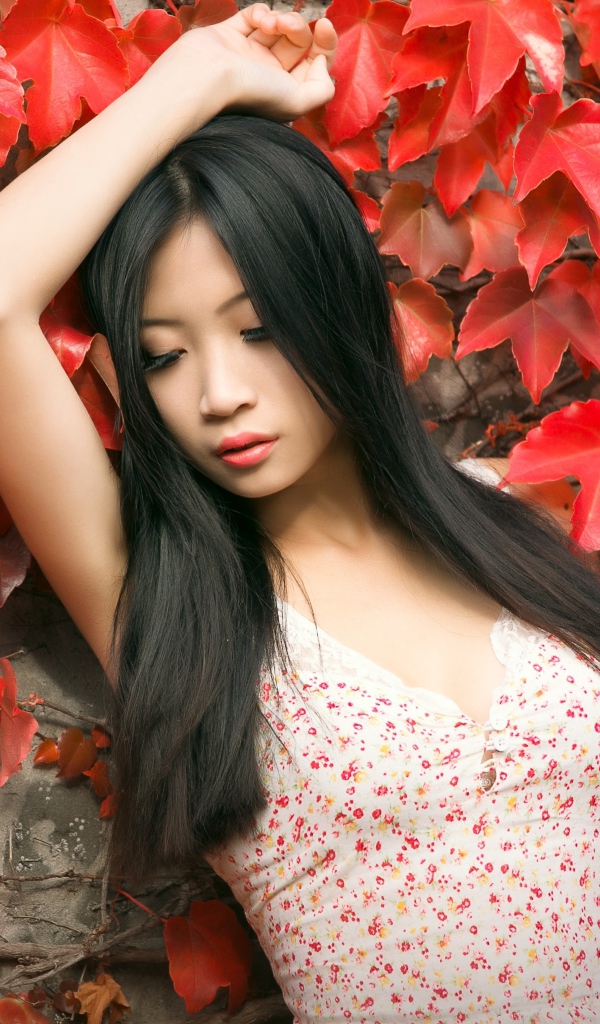 Молодая девушка азиатка стоит у стены с красными листьями