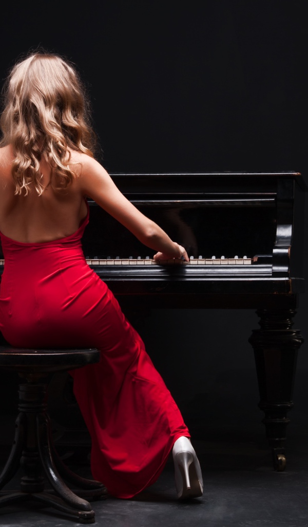 Молодая девушка в красном платье играет на пианино