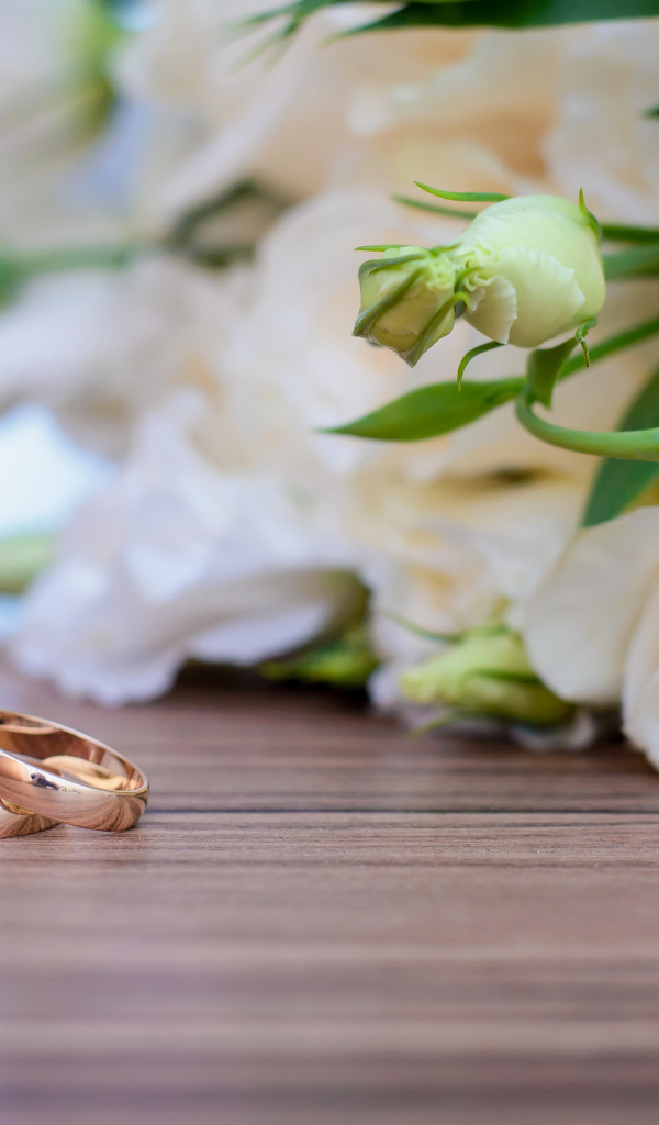 Букет белых роз на столе с золотыми обручальными кольцами
