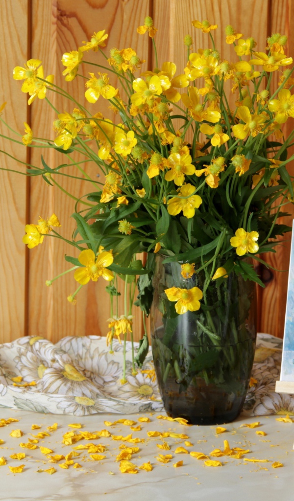 Букет желтых полевых лютиков в стеклянной вазе на столе с картиной