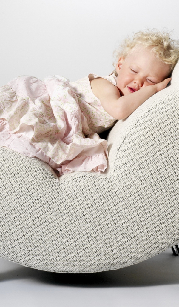 Маленькая девочка в розовом платье спит в кресле