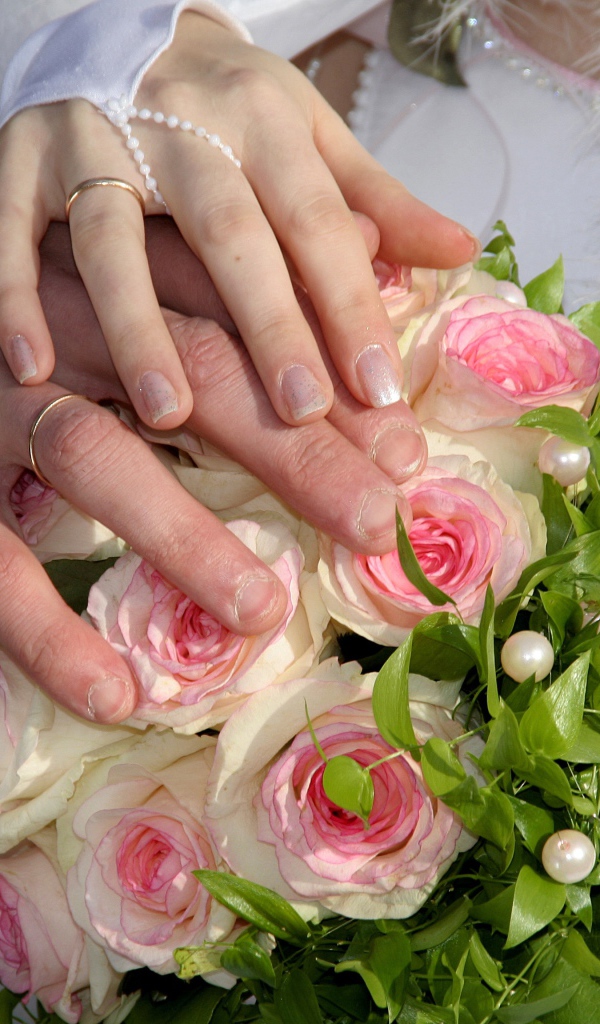 Руки жениха и невесты на букете с розовыми розами