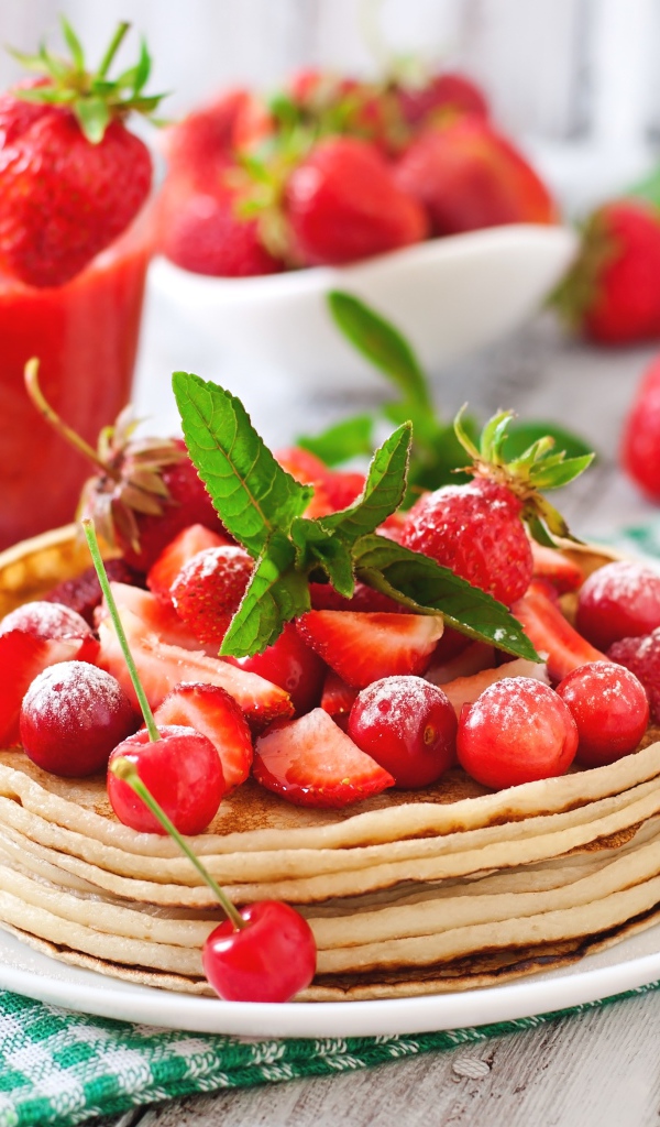 Блины с ягодами клубники  и черешни на белой тарелке
