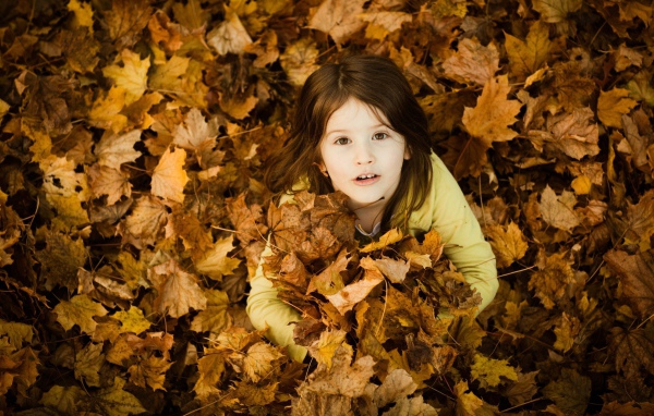 Девочка зарылась в опавшие листья