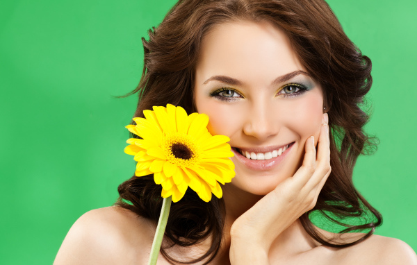 Девушка с красивой улыбкой и цветком желтой герберы в руках