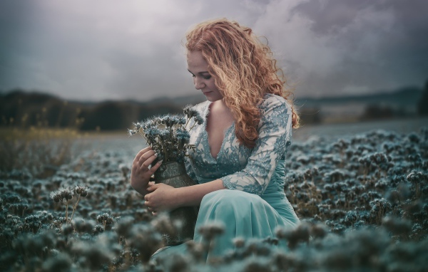 Молодая девушка собирает в кувшин голубые полевые цветы