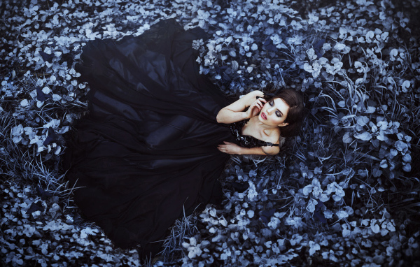 Молодая девушка модель с красивом черном платье лежит на траве