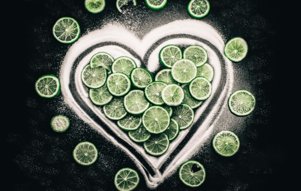 Сердце из сахара и кружочков  зеленого лайма на черном фоне