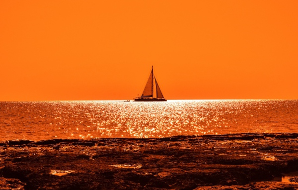 Парусная лодка на горизонте в океане на закате солнца