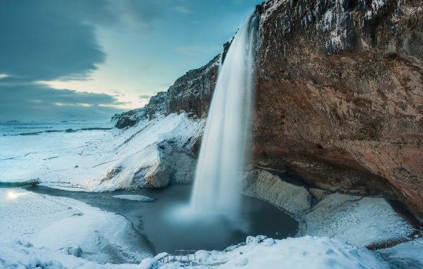 Водопад стекает с утеса на фоне заснеженной природы, Исландия