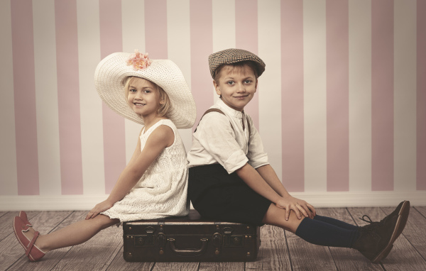 Девочка в большой белой шляпе и мальчик сидят на чемодане