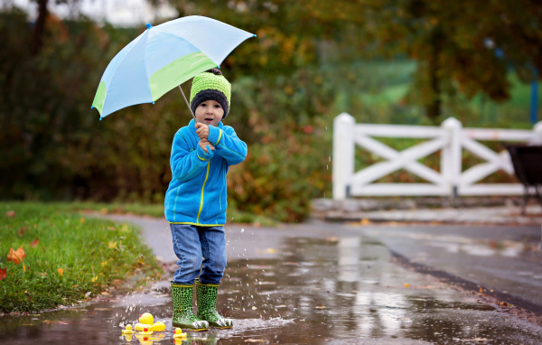 Маленький мальчик под зонтом гуляет по лужам