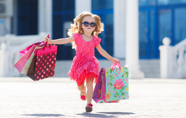 Маленькая девочка в розовом платье бежит с покупками из магазина