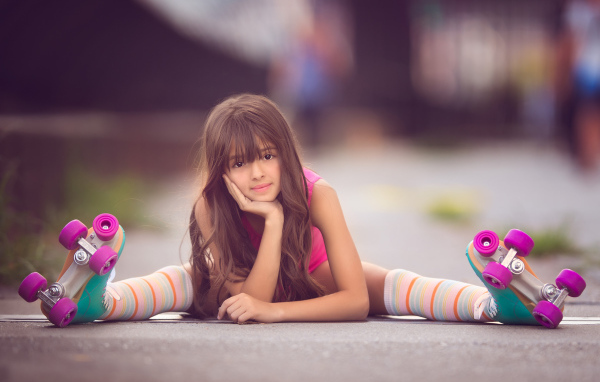 Маленькая девочка сидит на дороге в роликах