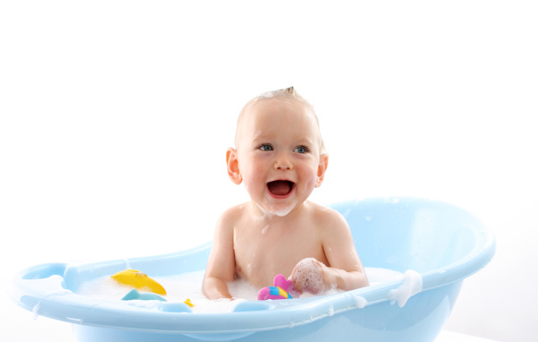 Улыбающийся грудной ребенок сидит в синей ванночке на белом фоне