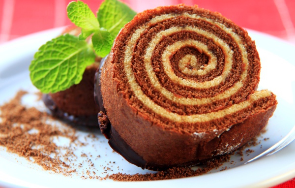 Кусок сладкого рулета с шоколадом и листом мяты на тарелке