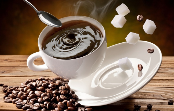 White cup with coffee falls on a table with coffee beans