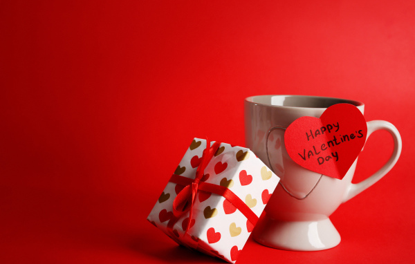 Чашка с подарком и валентинкой на красном фоне на 14 февраля