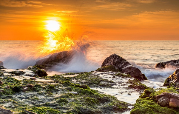The surging waves in the sea are beating against the stones at sunset