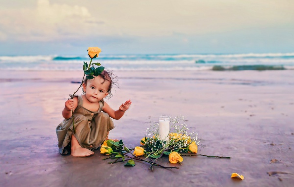 Маленькая девочка сидит на песке с розами 