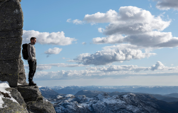 Мужчина стоит на краю скалы на фоне неба 
