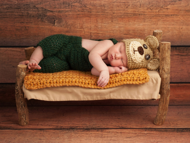 Новорожденный ребенок в костюме медвежонка спит на крошечной кровати