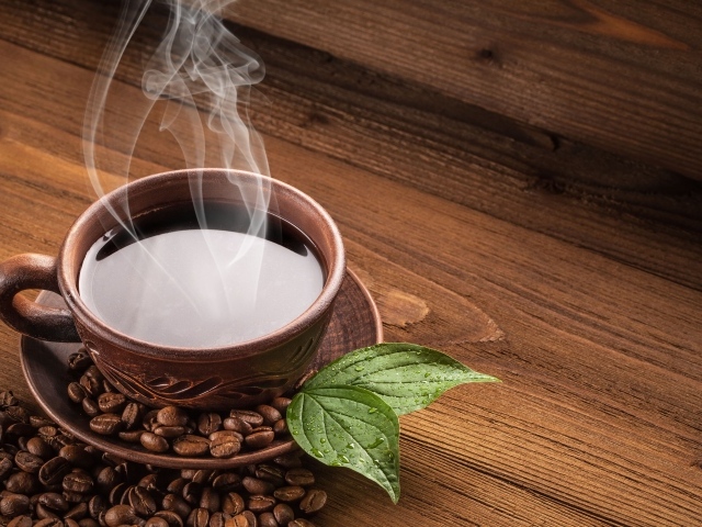 Чашка горячего кофе с зернами на деревянном столе