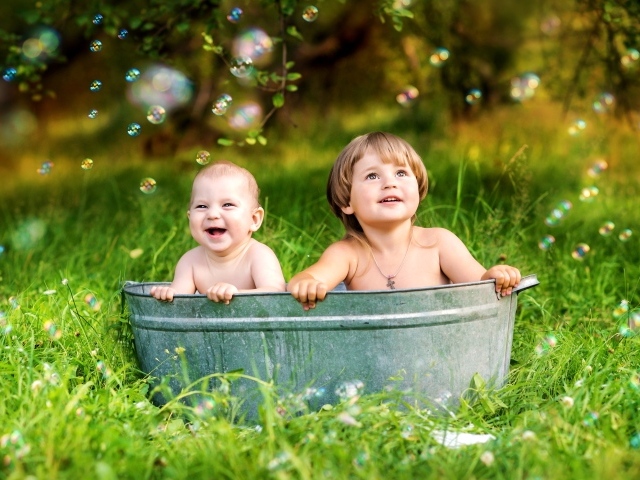 Два маленьких ребенка сидят в железном корыте на зеленой траве