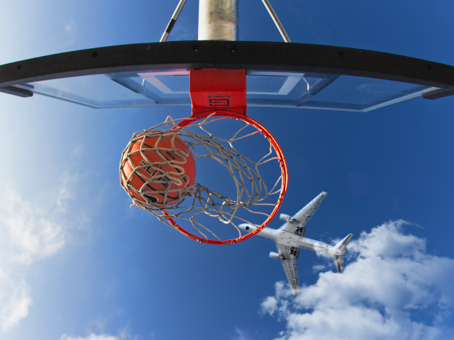 Самолет пролетает над баскетбольным кольцом в голубом небе 