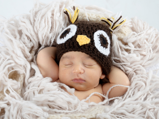 Маленький ребенок  в вязаной шапке спит на кровати 