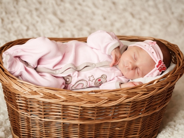 Маленькая новорожденная девочка в розовом костюме спит в корзине 