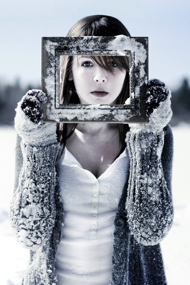 Девушка держит в руках фоторамку в снегу