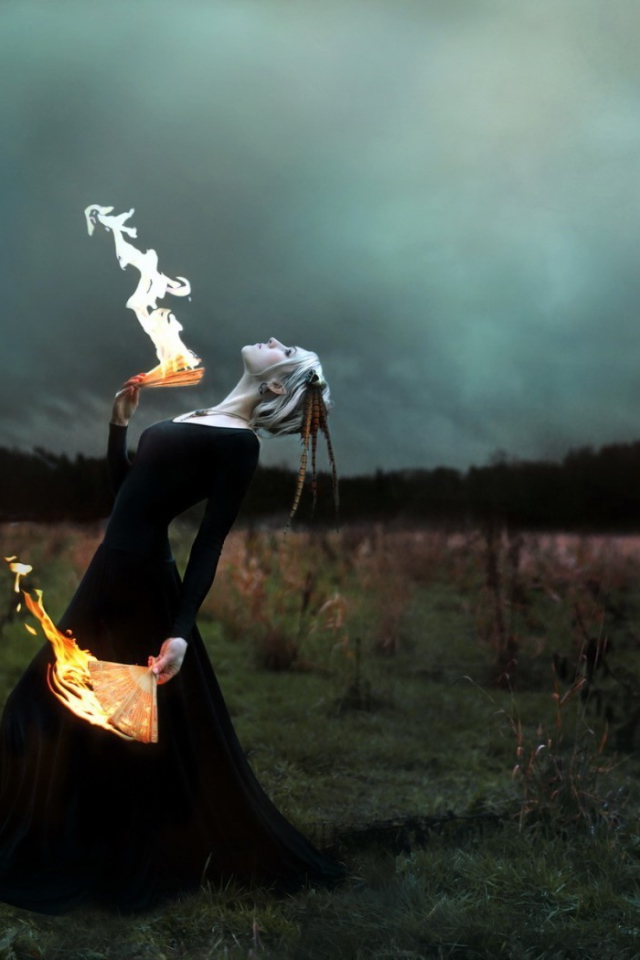 Девушка в черном платье играет с огнем