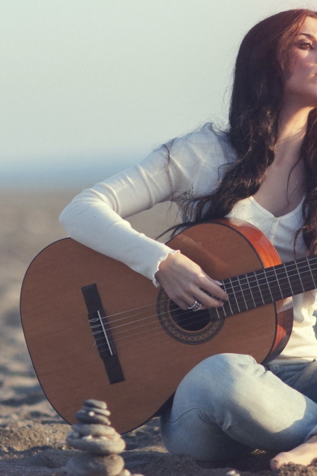 Греческая девушка сидит с гитарой на пляже
