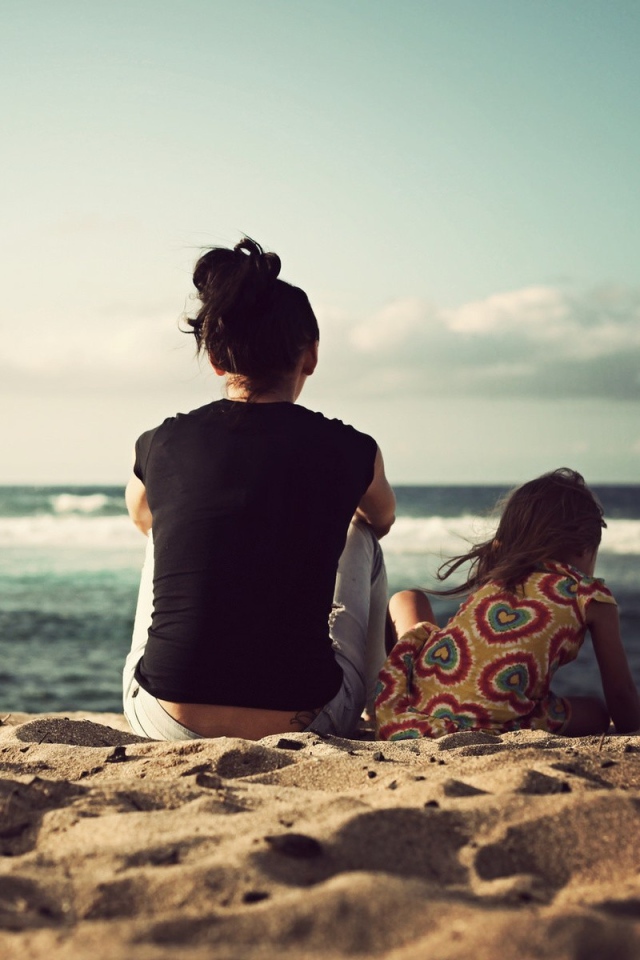 Женщина с дочкой сидят на песке на берегу моря
