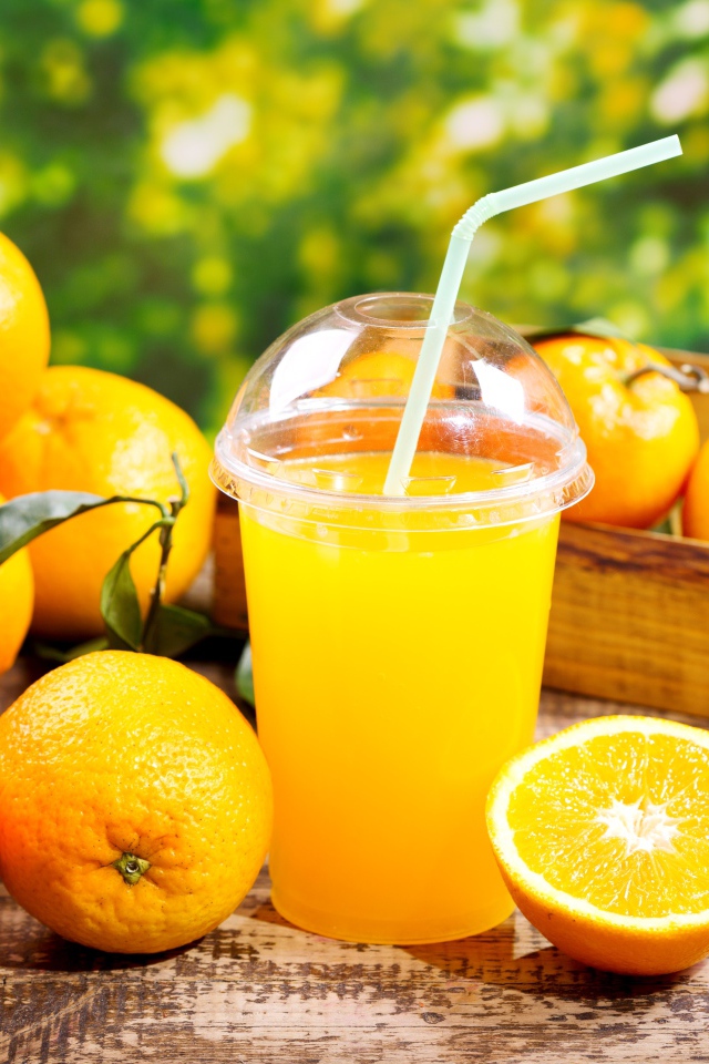 Стакан апельсинового сока с трубочкой на столе со свежими апельсинами