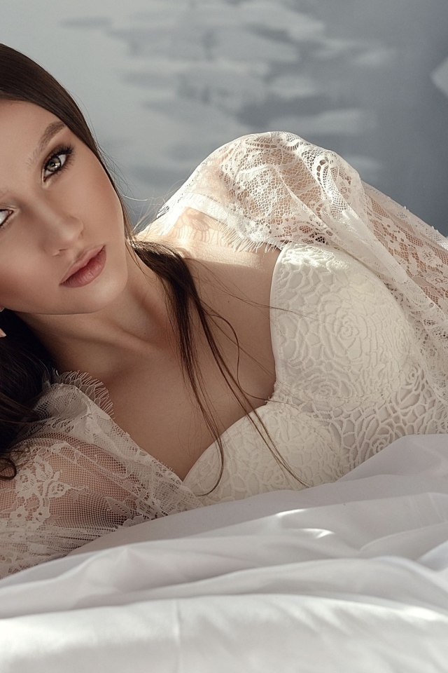 Красивая девушка брюнетка лежит на кровати в белом платье