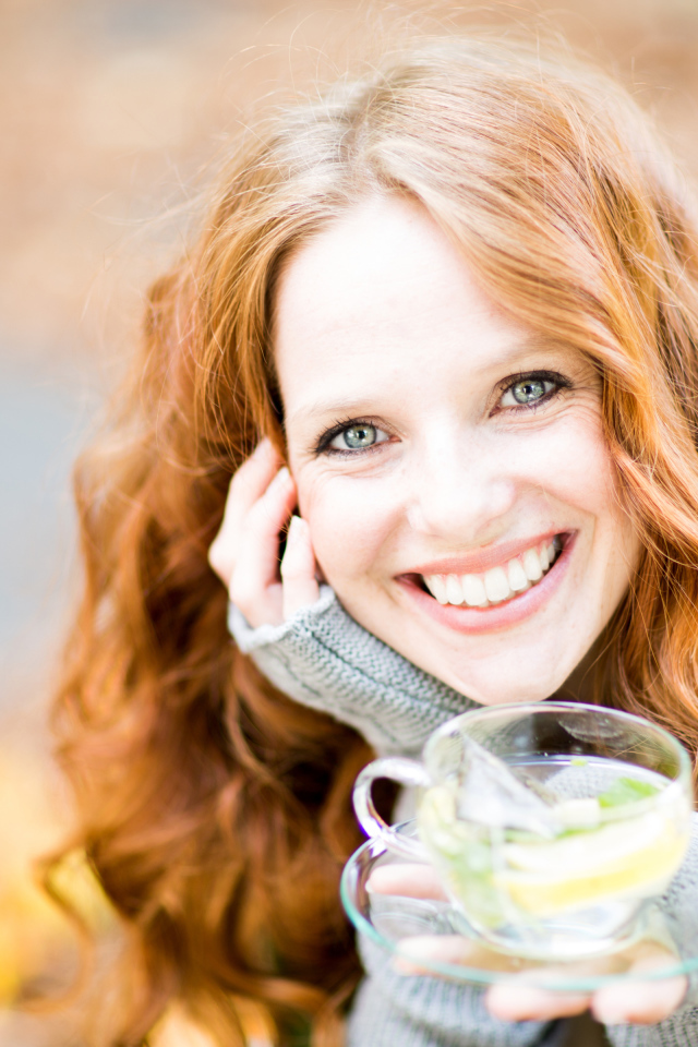 Smiling red-haired girl with a cup of tea in hand
