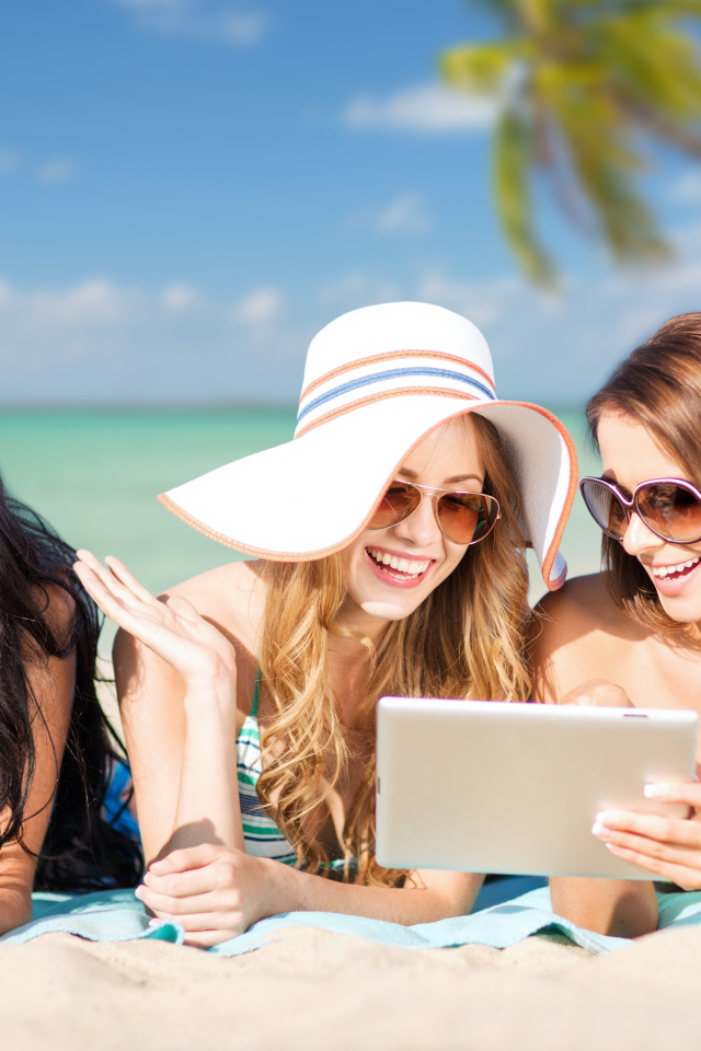 Три улыбающиеся девушки загорают на пляже с планшетами в руках