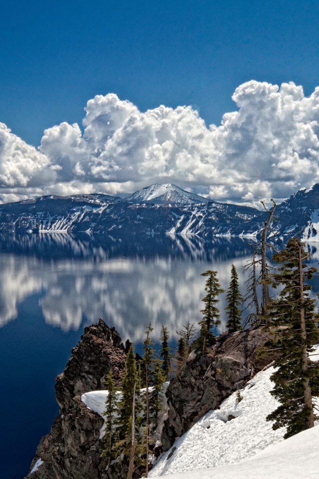 Белые облака отражаются в чистой воде озера у горного хребта