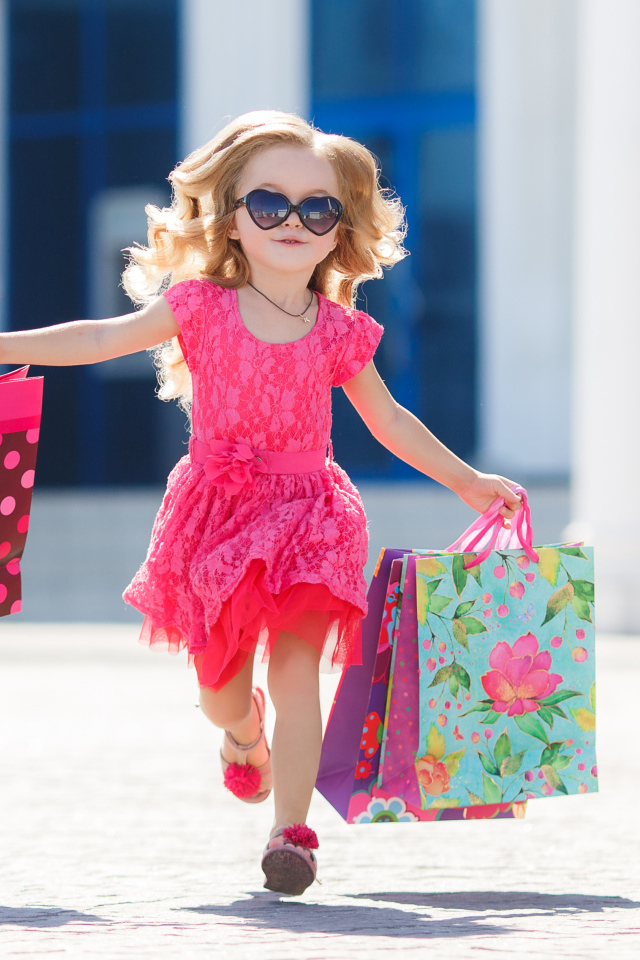 Маленькая девочка в розовом платье бежит с покупками из магазина